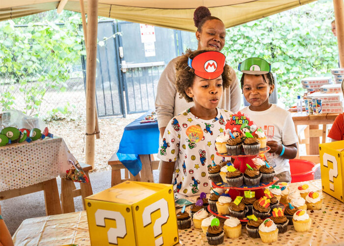 Los niños de cumpleaños sonrientes soplan las velas con sus padres en segundo plano.