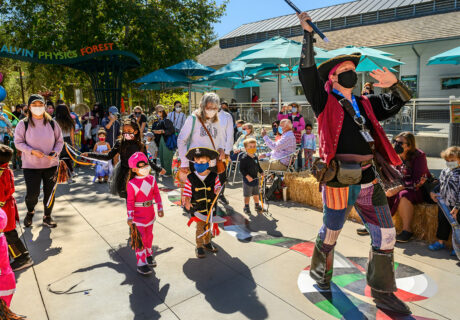 a children's halloween parade led by an adult in a pirate costume