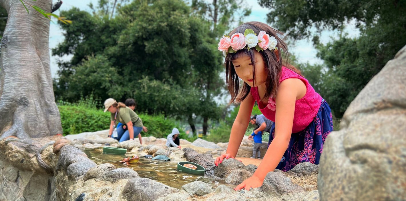 child with flowers in hair and magenta shirt plays with water