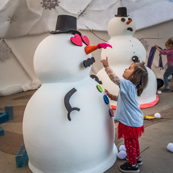 Small child reach up at pretend snowman