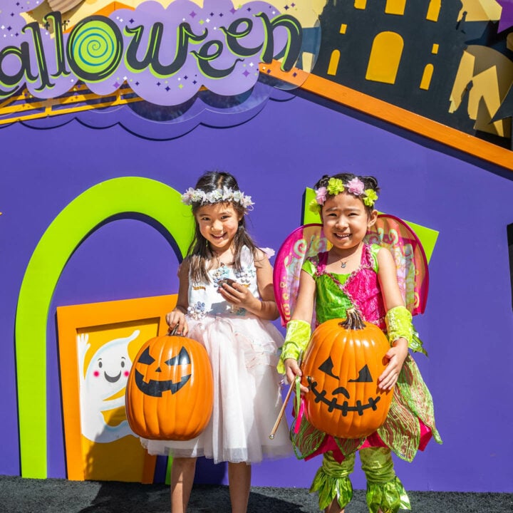 two costumed girls hold jack o'lanterns