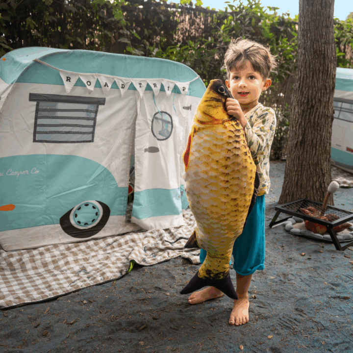 child with giant plush fish posing in front of play trailer