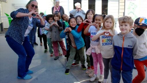 Children and teachers hold up their hands in the shape of hearts