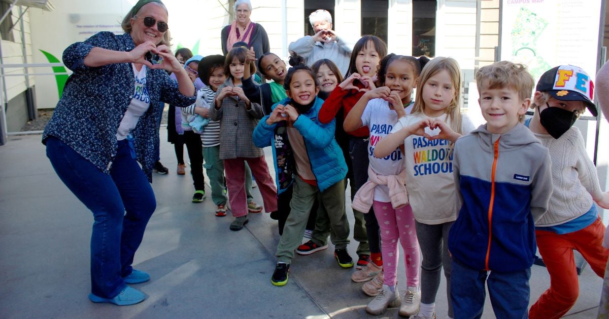 Children and teachers hold up their hands in the shape of hearts