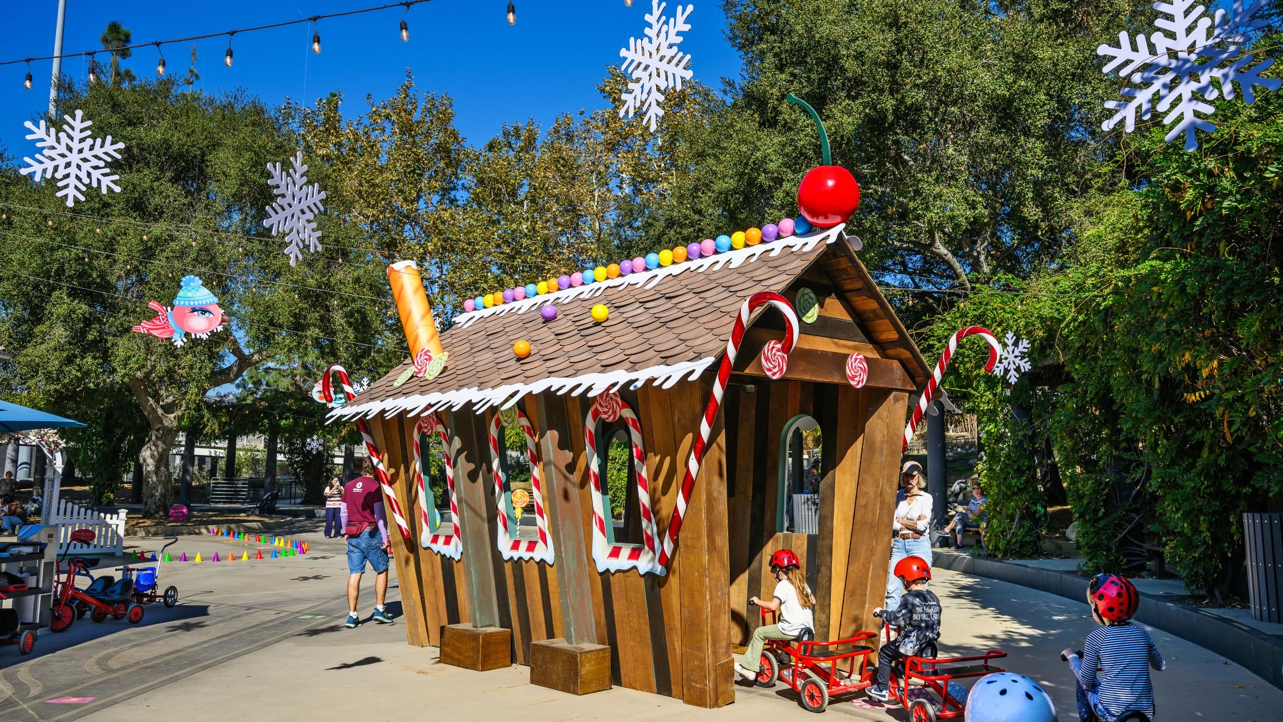 Children riding trikes through a gingerbread house
